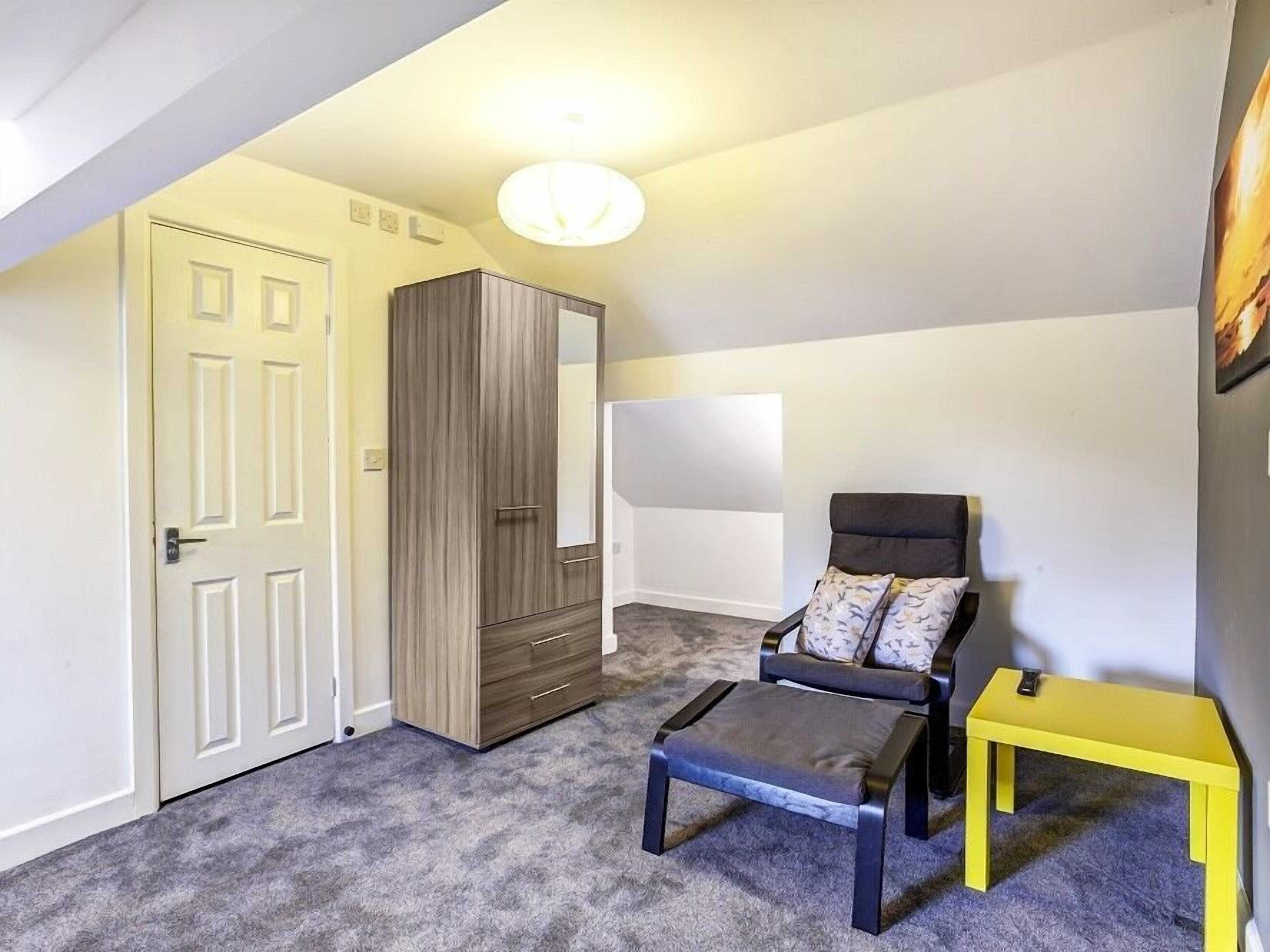 A bedroom with a bed, a chair, a small table, a wardrobe, and a door.