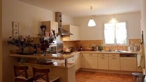 A kitchen with a central island, white cabinets, a stove, and a window with blinds.