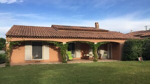 A house with a tiled roof, a covered patio with chairs, and a well-maintained lawn.