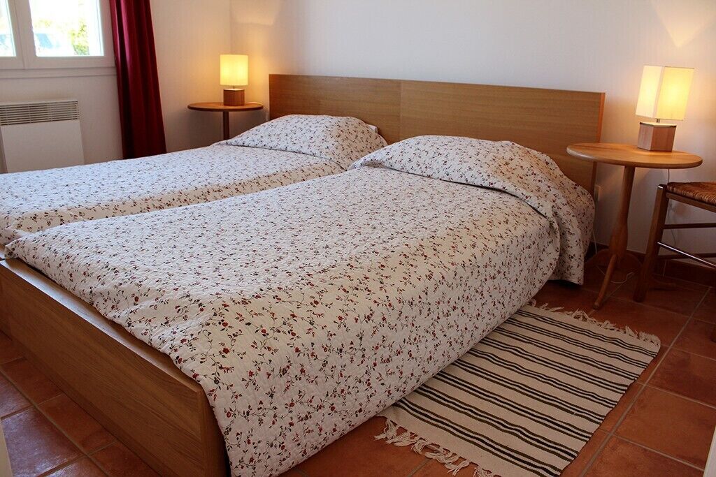 Un lit double avec une literie à motifs floraux, deux tables de chevet avec des lampes et un tapis à rayures.