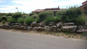A stone wall with large rocks and green shrubs in front of a building with a tiled roof.