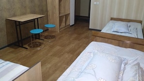 Une chambre avec un plancher en bois, un lit avec une literie à motifs floraux, une petite table avec des tabourets et une armoire.