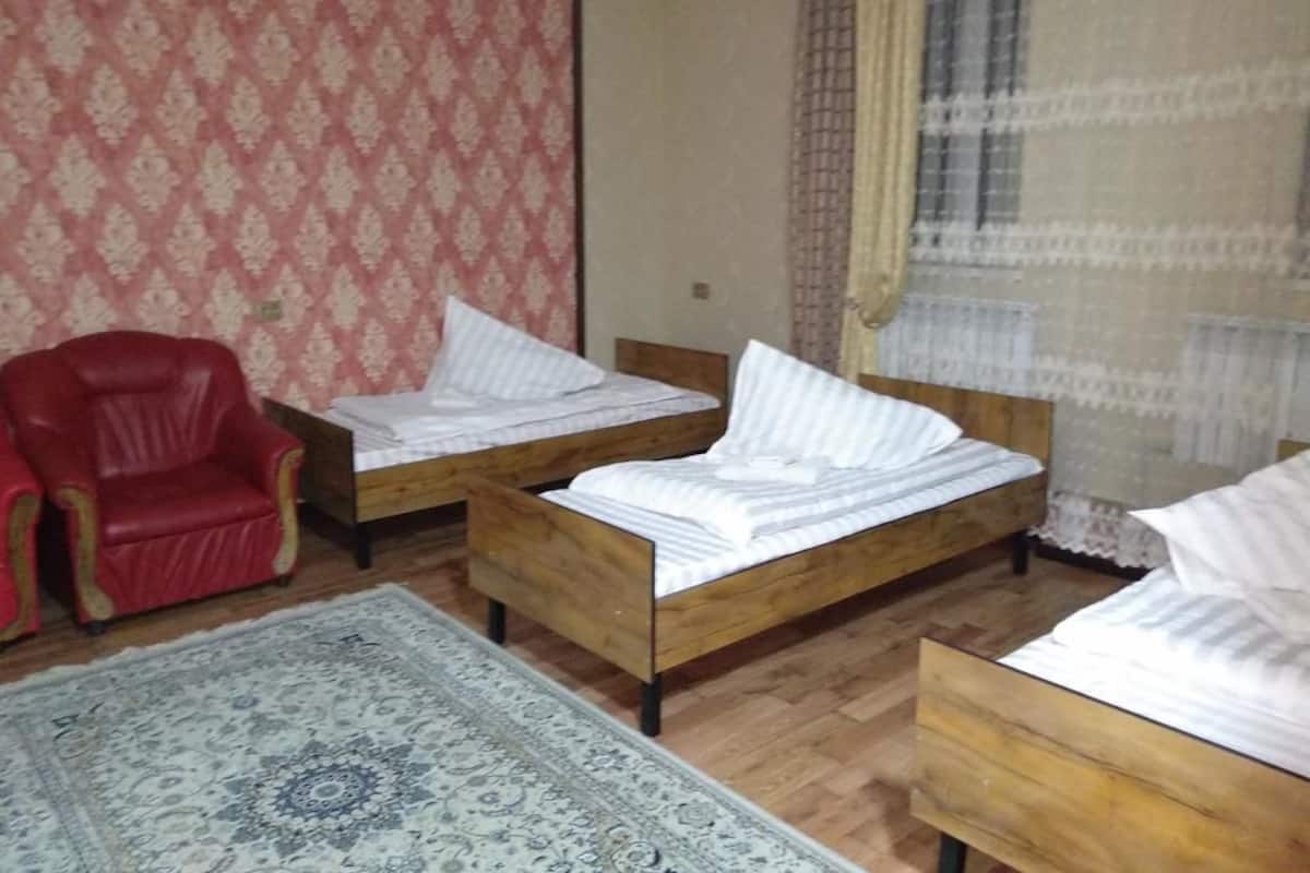 Una habitación con dos camas de madera, una silla roja y un tapete estampado.