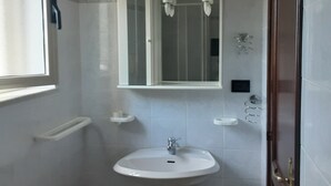 Ein Badezimmer mit einem Standwaschbecken, einem Spiegel darüber und einer kleinen Ablagefläche.
