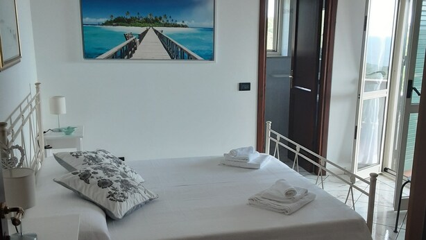 Ein Schlafzimmer mit Bett, Schreibtisch, einem Bild und Blick ins Freie.