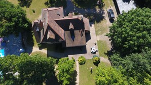 Vista aérea de una casa con techo inclinado, rodeada de árboles y un pequeño césped.