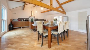 A spacious dining area with a wooden table and chairs, a kitchen in the background, and a high ceiling with exposed beams. - The Loft-Stylish Stay – Sleeps 6 (Southport)