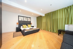 Une chambre moderne avec un lit, des tables de chevet, une petite table et un rideau vert.