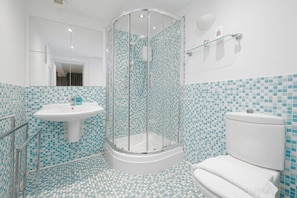 Une salle de bain avec une douche à parois de verre, un lavabo sur colonne et des toilettes.