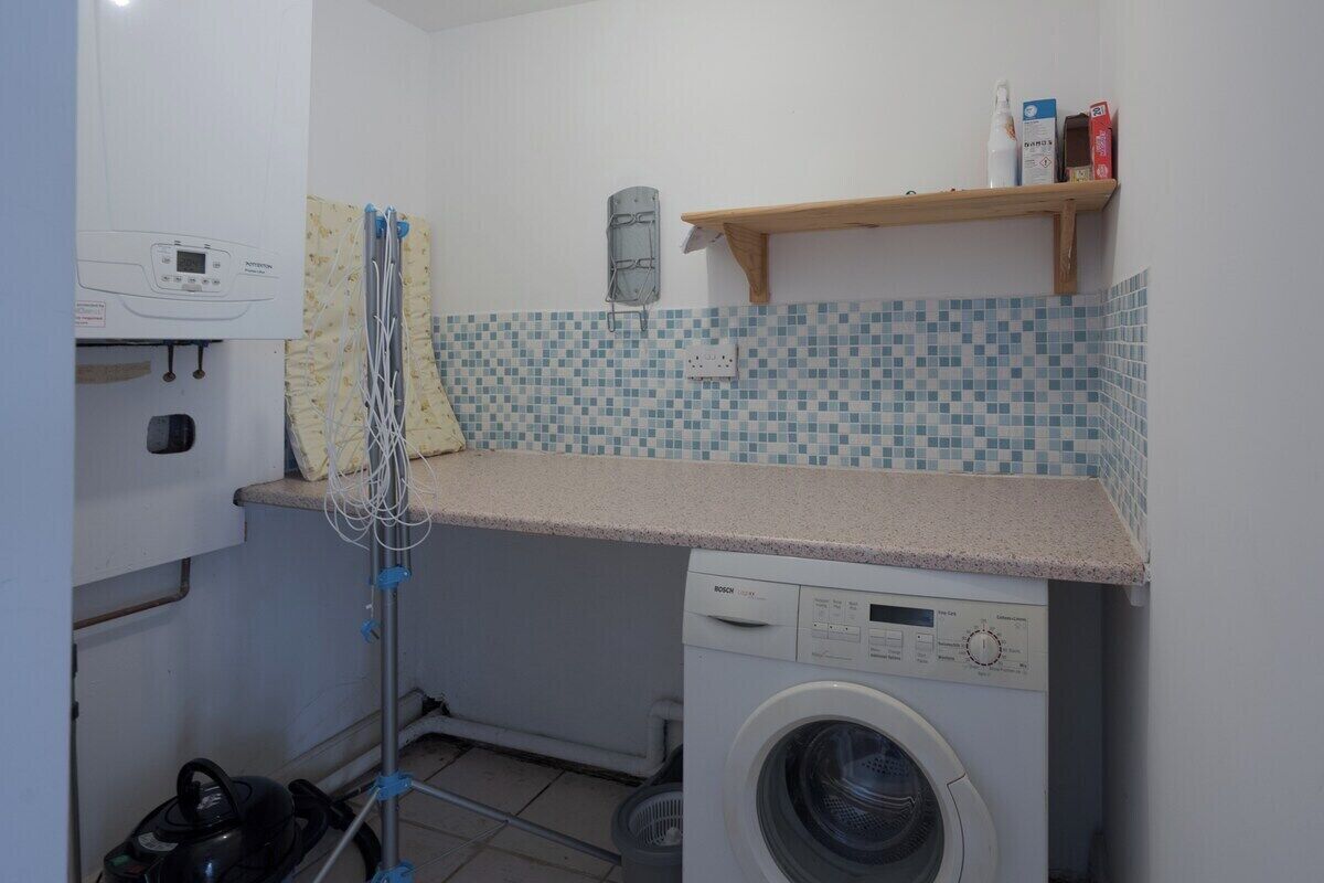 A compact laundry room with a Bosch washing machine, a drying rack, and a small shelf with toiletries.