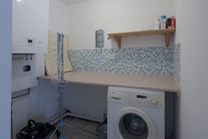 A compact laundry room with a Bosch washing machine, a drying rack, and a small shelf with toiletries.