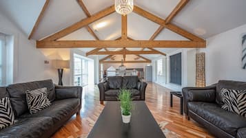A spacious living area with high ceilings and exposed wooden beams, a central coffee table with a plant, and leather sofas with patterned cushions.