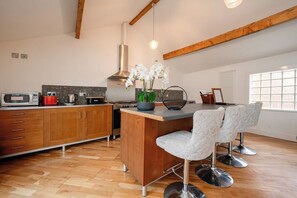 A modern kitchen with wooden cabinets, a central island, bar stools, and a hanging light fixture.