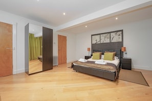 A modern bedroom with a large bed, a mirror, a nightstand, and a wall-mounted artwork.