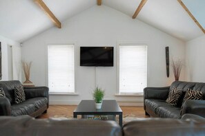 A living room with a black leather sofa, a coffee table, and a flat-screen TV mounted on the wall.