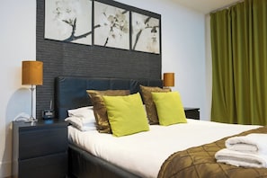 A hotel room with a bed, two bedside lamps, a nightstand, and a wall-mounted artwork.
