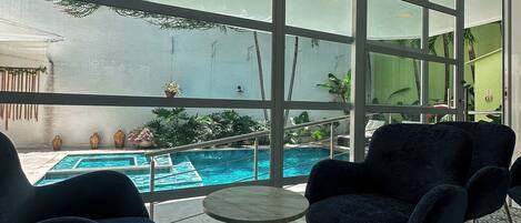 A modern indoor space with large windows, a pool, and dark blue chairs.