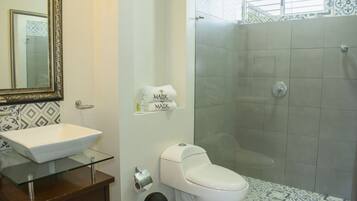 Un baño con lavamanos de vidrio, inodoro y zona de ducha.