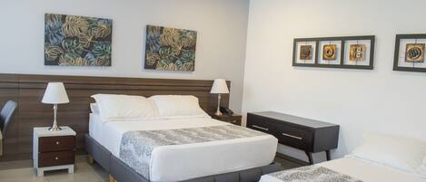 A hotel room with a bed, bedside tables, a desk, and artwork on the walls.