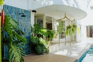 Un área de piscina interior moderna con pared de azulejos azules, grandes plantas tropicales y una disposición de plantas colgantes.