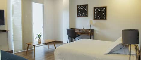 A hotel room with a bed, a desk, a chair, a TV, and artwork on the wall.
