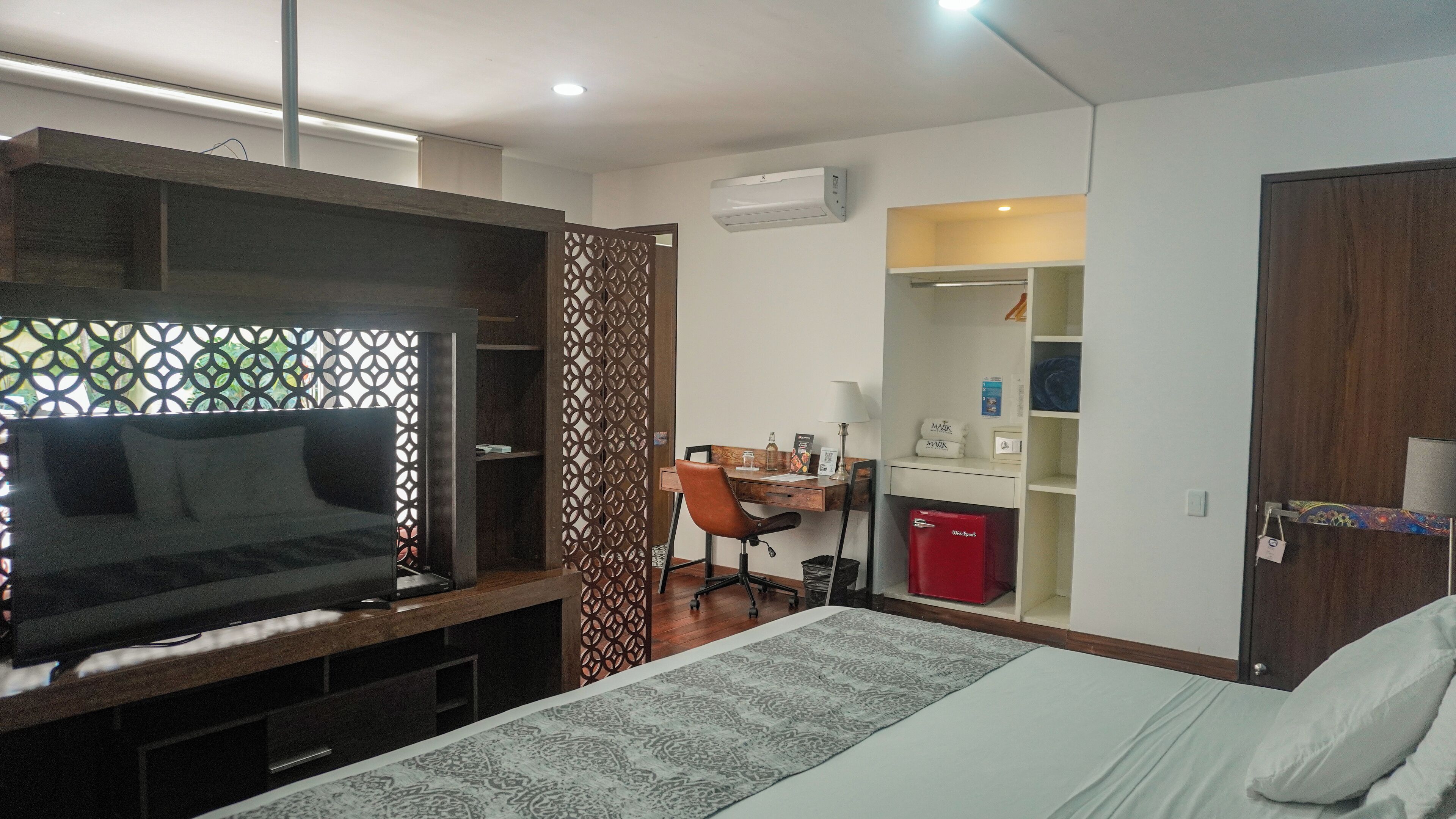 A compact hotel room with a bed, a desk, a chair, a TV, and a wardrobe.