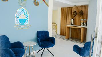 Een kamer met twee blauwe stoelen, een klein rond tafeltje en een wand met decoratieve kunst.