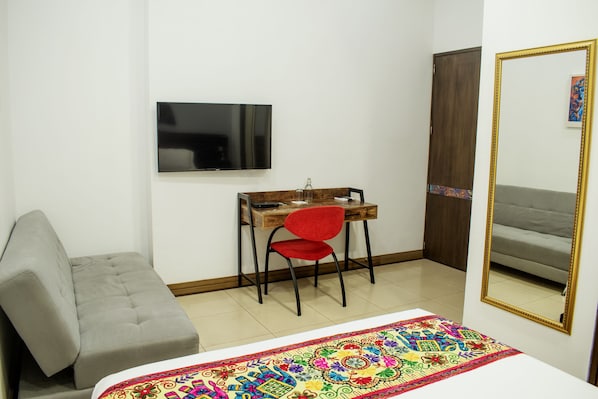 A bedroom with a bed, a desk with a chair, a television, and a wardrobe.