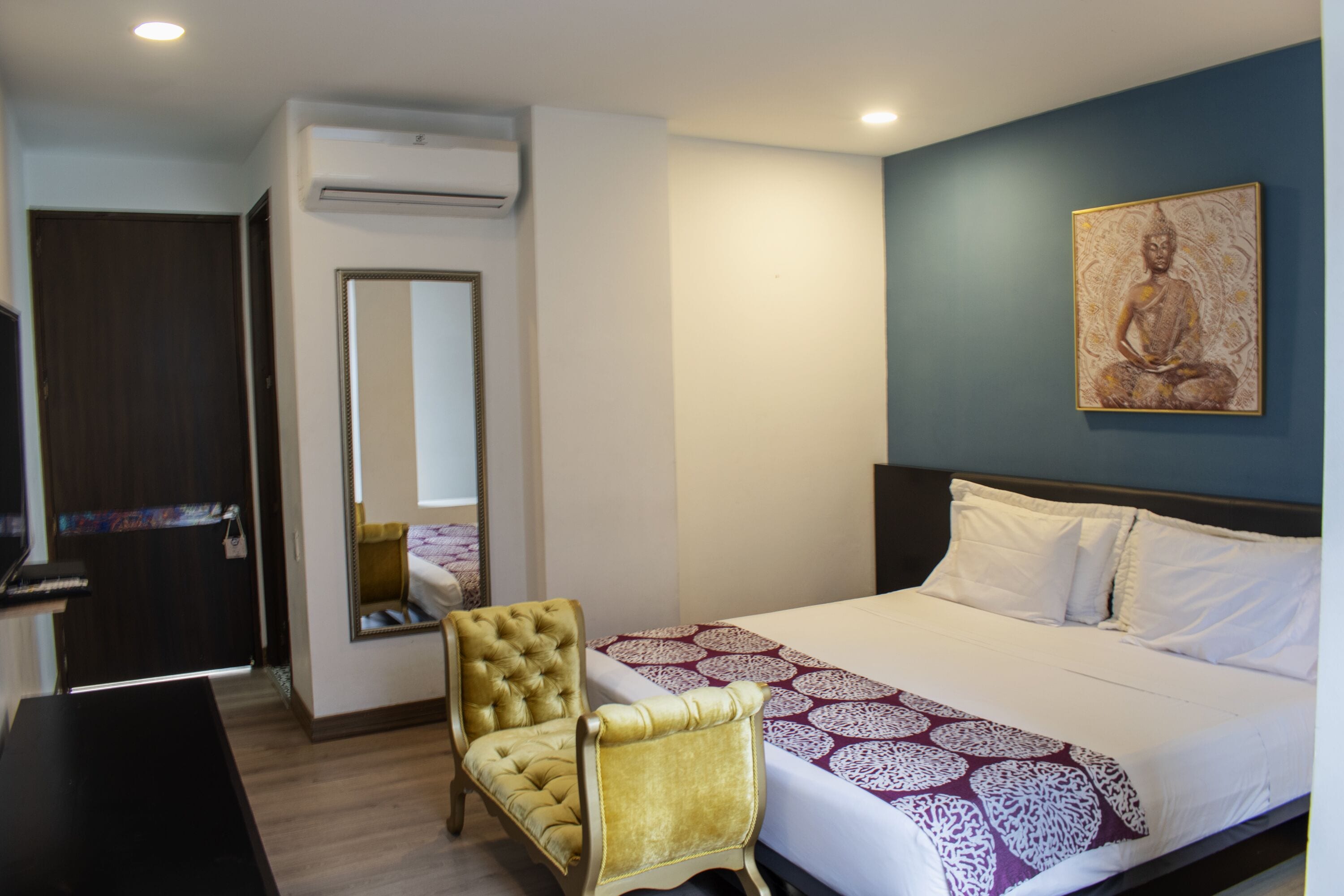 A hotel room with a bed, a chair, a television, and a wall-mounted artwork.