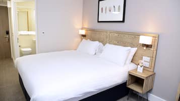 A neatly made bed with white linens, a wooden headboard, and two bedside lamps.