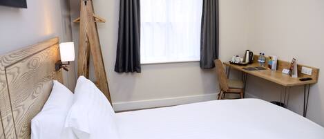 A hotel room with a bed, a desk, a chair, a coat rack, and a window with curtains.