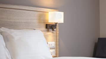Hotellihuone, jossa on puinen sängynpääty, yöpöytälamppu ja valkoinen sänky.