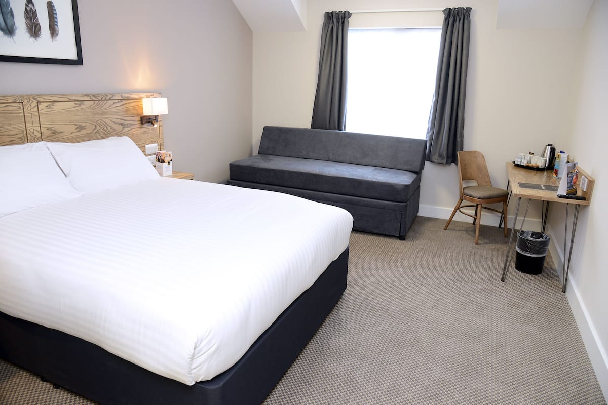 A hotel room with a bed, a sofa, a desk, and a chair.