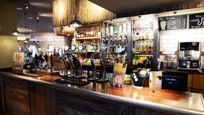 A bar area with multiple taps, shelves stocked with bottles, and a menu board listing hot drinks.