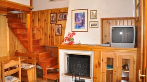 Eine Holztreppe führt zu einem Schlafbereich mit Kamin, Holzmöbeln und gerahmten Bildern an den Wänden.