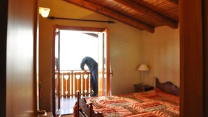 Ein Schlafzimmer mit Holzboden, einem Bett mit gemustertem Überwurf, einem Nachttisch mit Lampe und Blick auf einen Balkon.