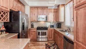 Una cocina con gabinetes de madera, electrodomésticos de acero inoxidable, encimera de granito y alfombra estampada.