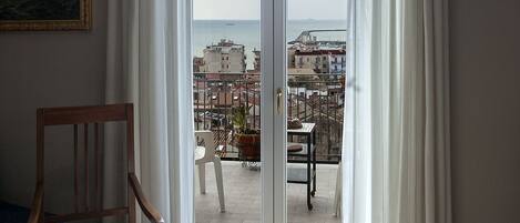A room with a view of the sea, a wooden chair, a table, and a potted plant.
