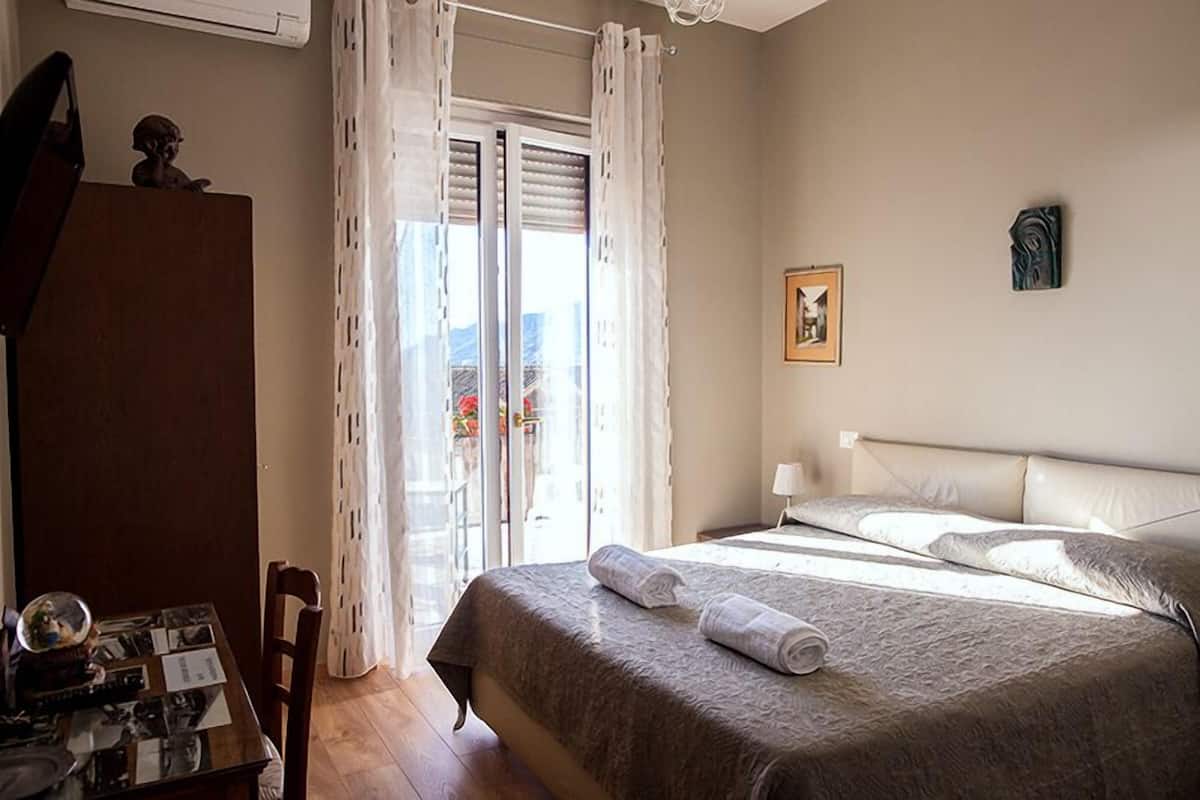 A hotel room with a bed, a desk with a chair, and a window with curtains.