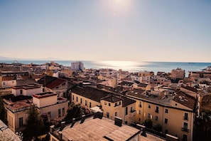 Un paisaje urbano costero con edificios históricos, cielo despejado y el mar al fondo.