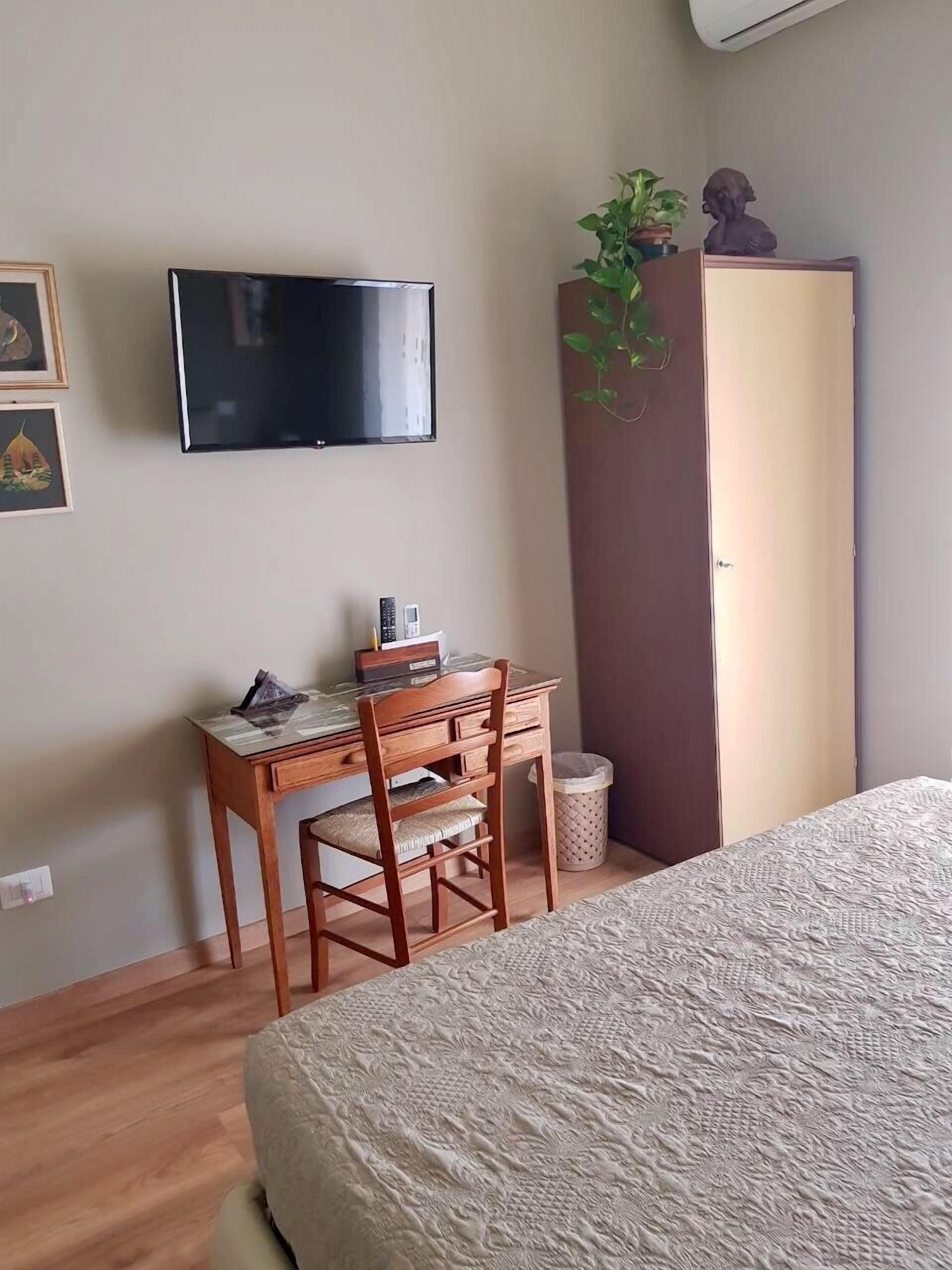 Ein Schlafzimmer mit einem Bett, einem Schreibtisch mit Stuhl, einem Fernseher, einem Kleiderschrank und einer Zimmerpflanze.