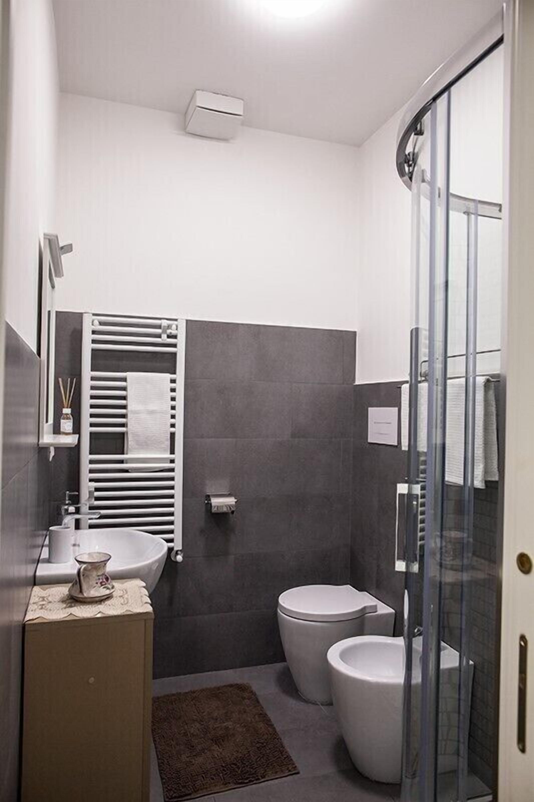 Une salle de bain moderne avec une douche à parois de verre, un lavabo blanc et deux toilettes.