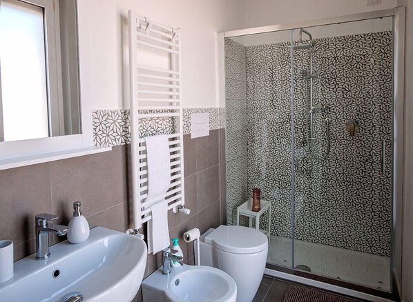 A bathroom with two sinks, a toilet, a shower with a glass door, and patterned tiles. - B&b Armonia (Salerno)