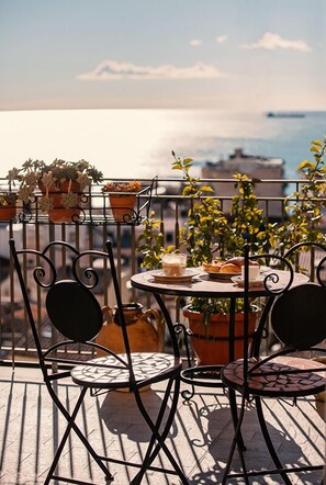 A terrace with a table and chairs, potted plants, and a view of the sea. - B&b Armonia (Salerno)