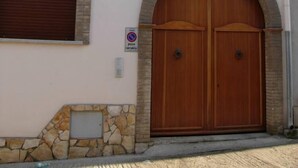 Un bâtiment doté d’une grande porte à double battant en bois, de deux fenêtres avec volets et d’un socle en pierre.