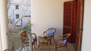 Un balcon avec des fauteuils en osier, une petite table et une porte en bois.