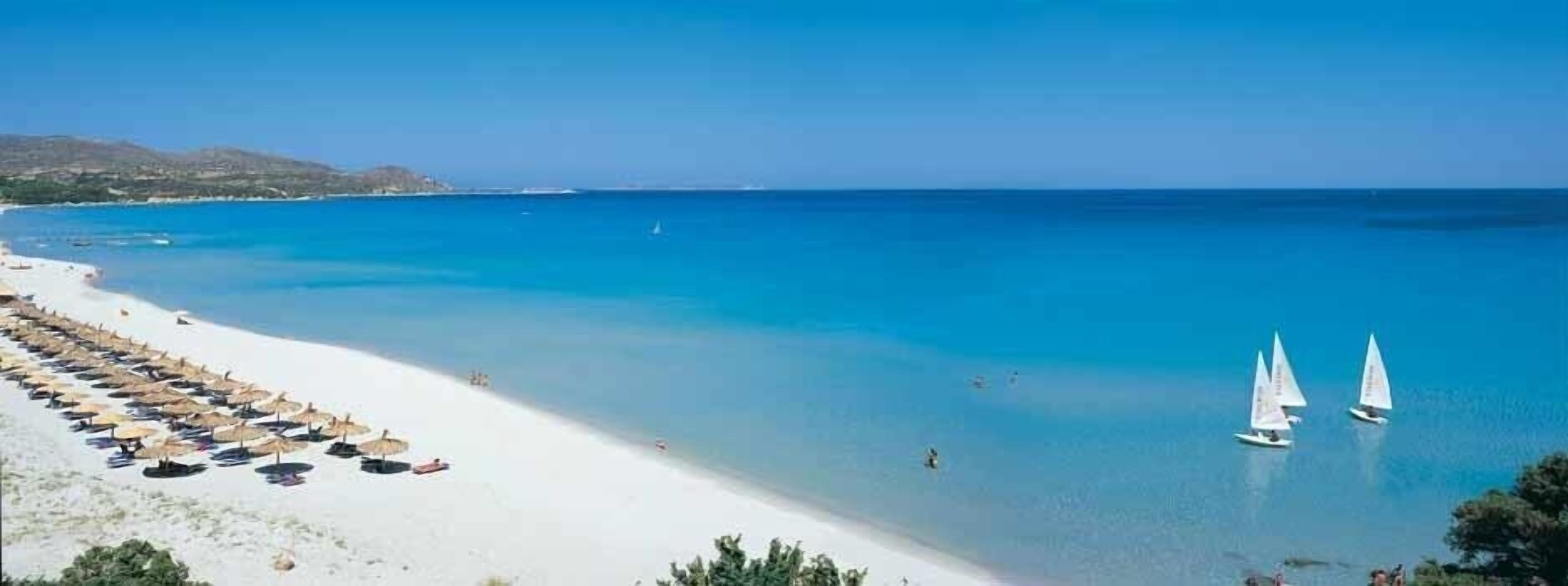 Une plage de sable blanc, avec une eau d’un bleu limpide et une rangée de parasols.