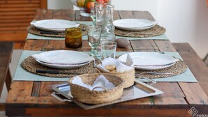 Ein Holztisch, gedeckt für eine Mahlzeit, mit Tellern, Gläsern und einer Obstschale im Hintergrund.
