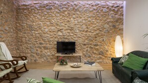 Ein Wohnzimmer mit einer Steinwand, einem Flachbildfernseher auf einem Holzboden, einem Sofa, einem Couchtisch und einem Sessel.