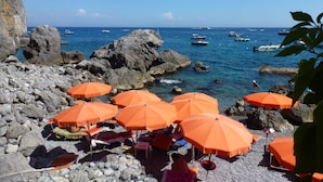 Ein felsiger Strand mit orangefarbenen Sonnenschirmen und entspannten Menschen.